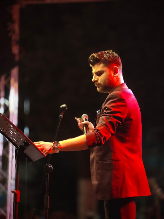 Orkun Kahriman konserde kırmızı sahne ışıkları altında mikrofonla